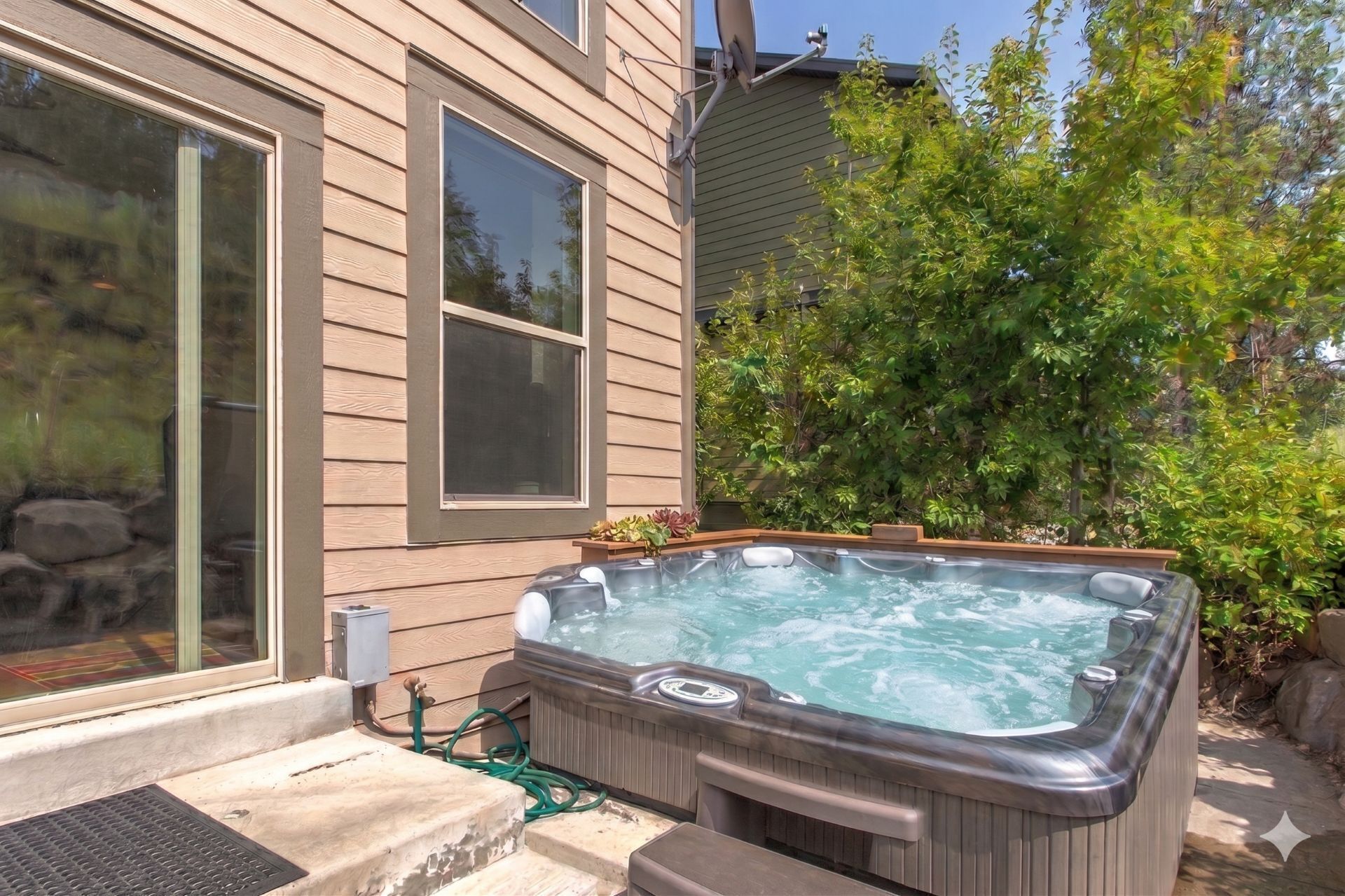 A hot tub in a backyard with a house, a window, and a garden.