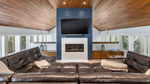 Un salon moderne avec un grand canapé en cuir, un téléviseur à écran plat fixé sur un mur bleu et une cheminée.