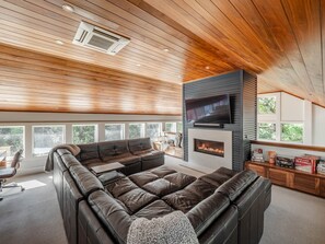 A modern living room with a leather sectional sofa, a flat-screen TV mounted on a black wall, and a fireplace.