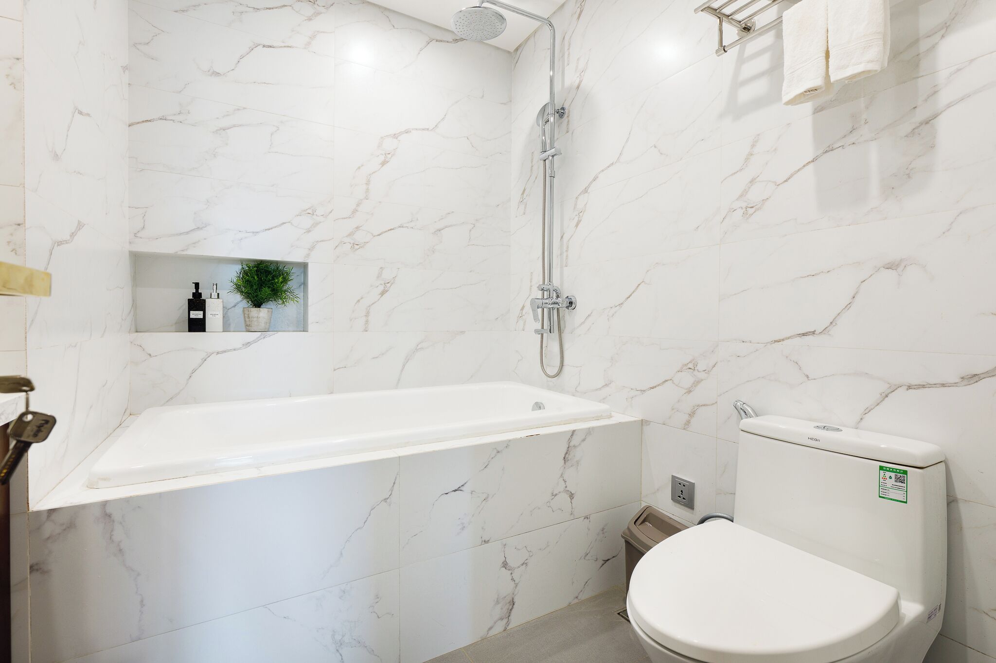 Une salle de bain avec un mur en marbre blanc, une baignoire sur pieds, des toilettes et une douche.