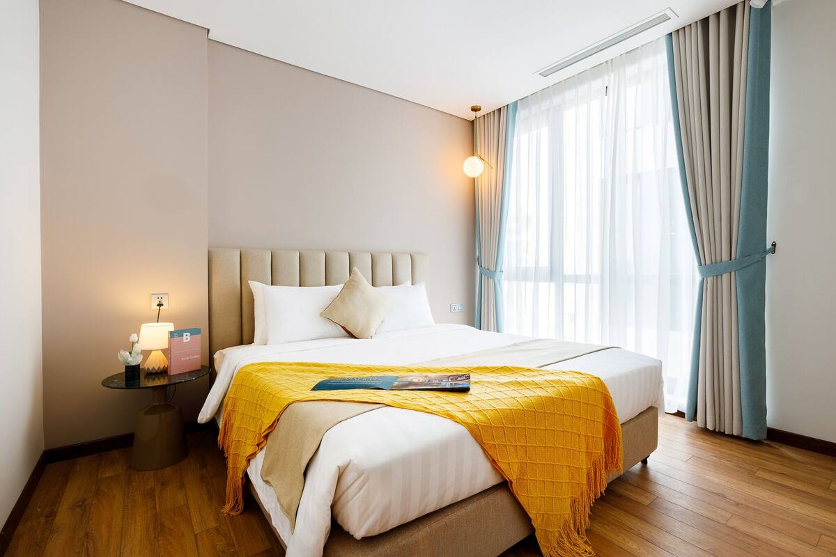 Een hotelkamer met een bed, nachtkastje, lamp en gordijnen.