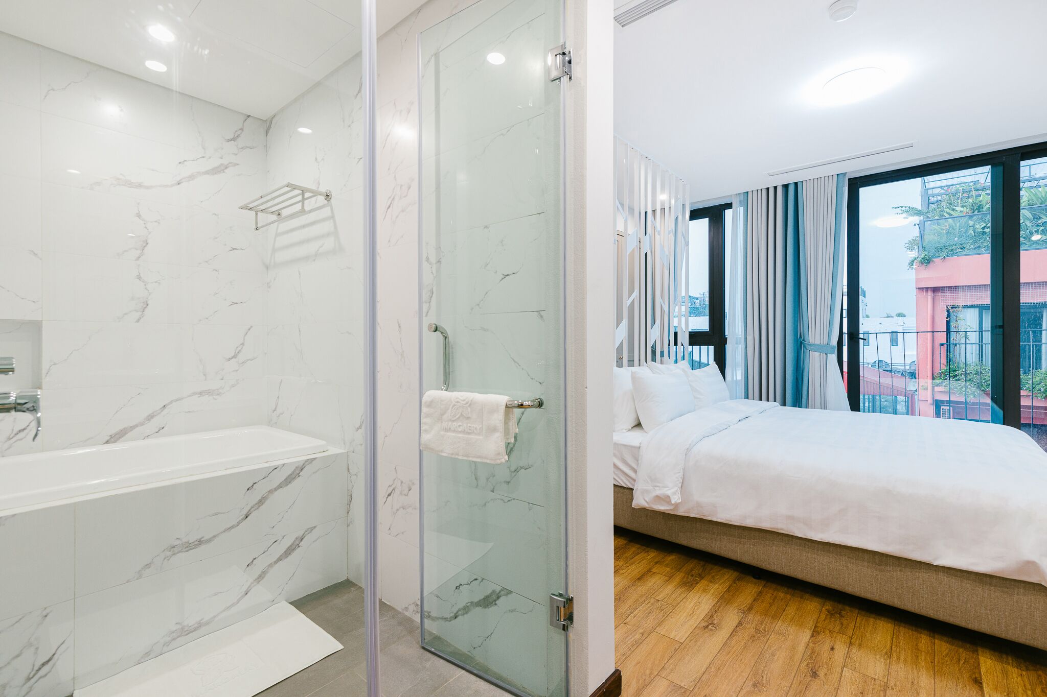 Ein modernes Badezimmer mit einer gläsernen Duschkabine und einer großen Badewanne. Das Schlafzimmer verfügt über ein großes Bett und bietet durch große Fenster einen Blick auf die Stadt.