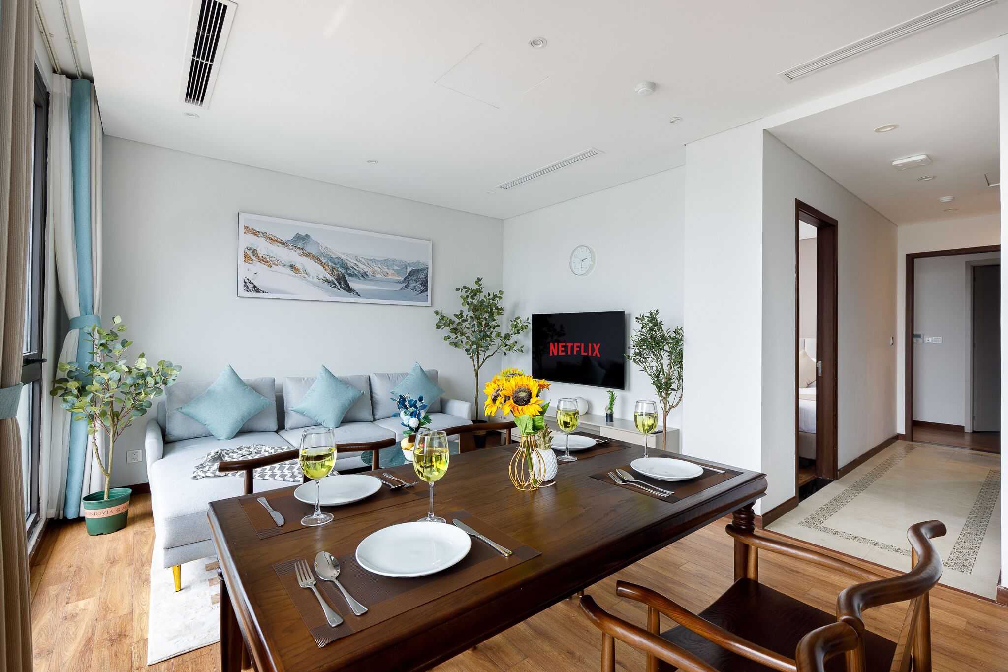 Un salon moderne comprenant un coin repas, un canapé, un téléviseur et une table à manger, le tout agrémenté de verres à vin et d’assiettes.