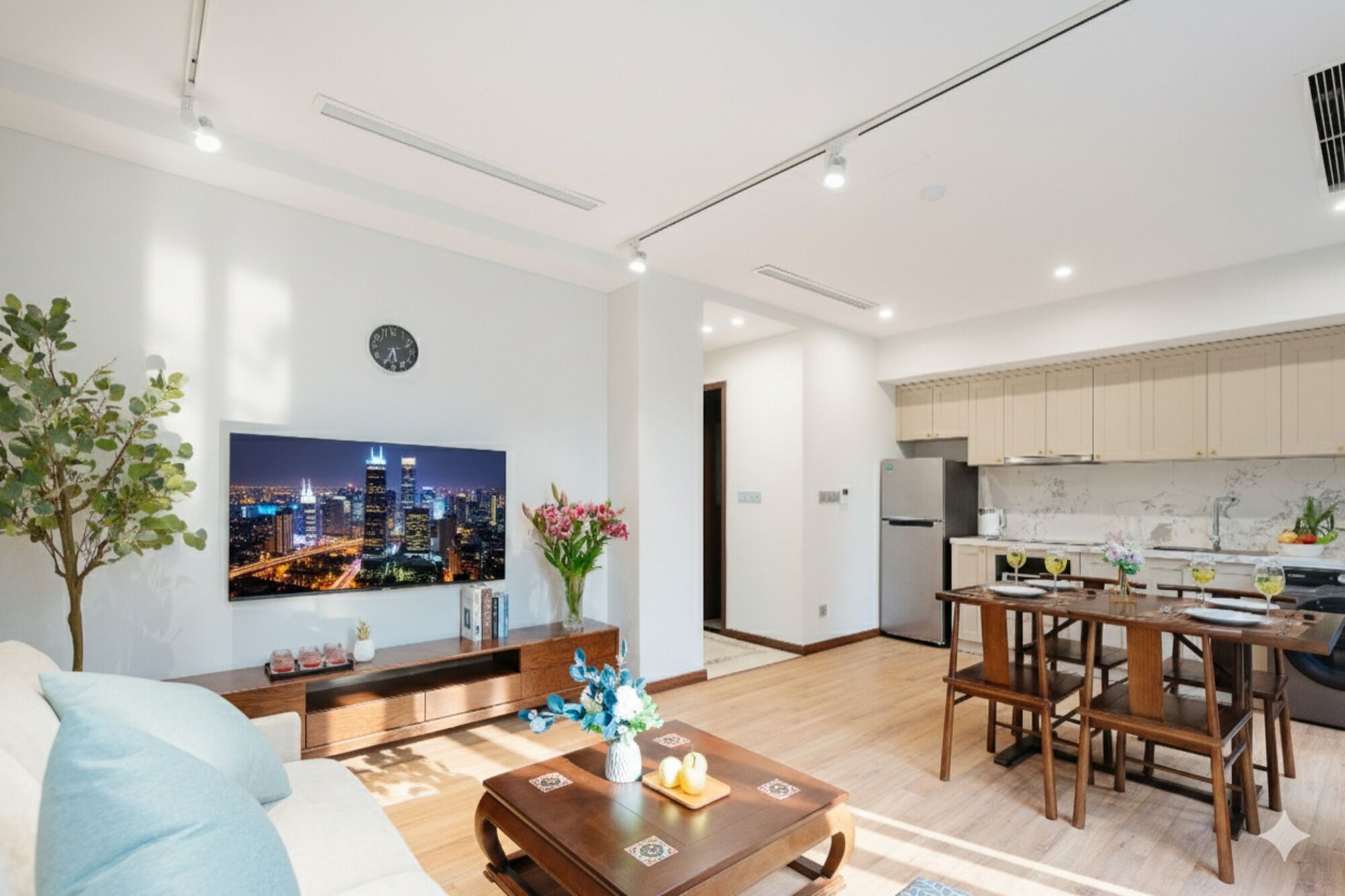 Eine moderne Wohnung mit Wohnzimmer, Essbereich und Küche. An der Wand hängt ein Stadtbild, außerdem befindet sich dort eine Uhr und eine Pflanze.