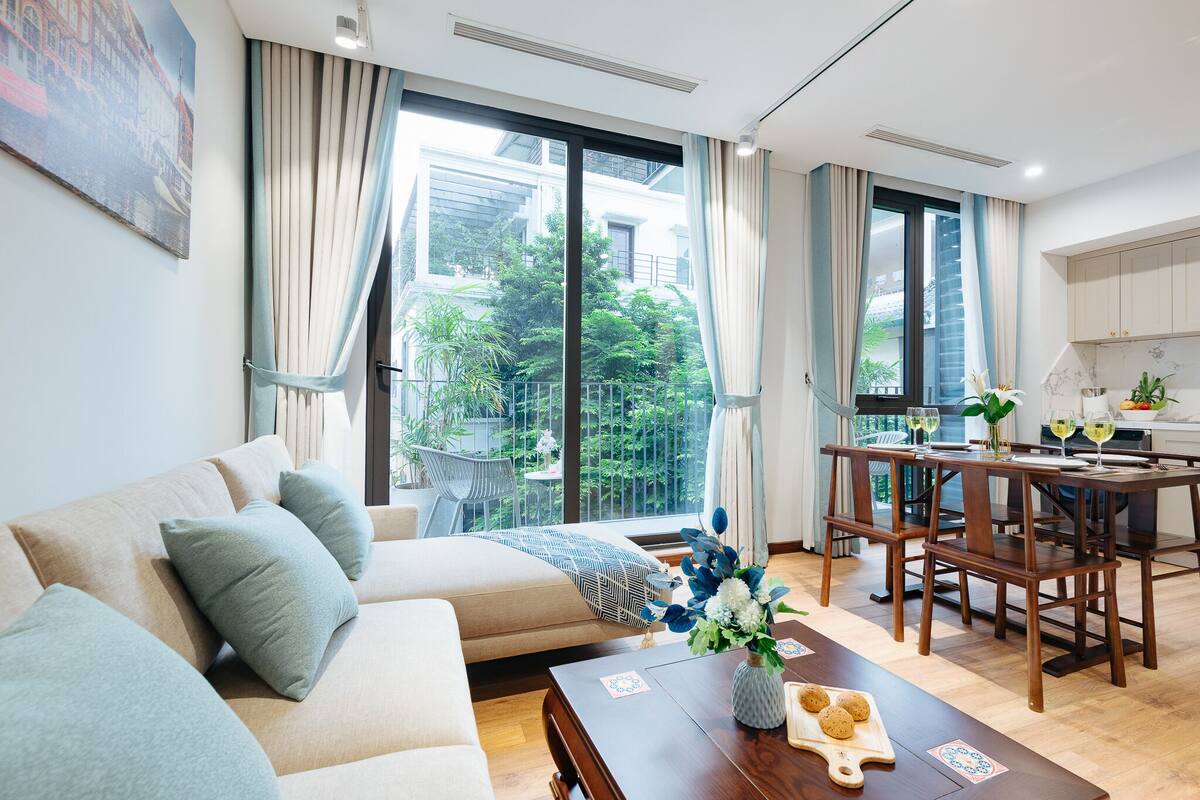 Een moderne woonkamer met een bank, eettafel en grote ramen met uitzicht op een tuin.
