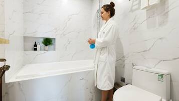 A bathroom with a marble wall, a bathtub, a toilet, and a shelf with toiletries.