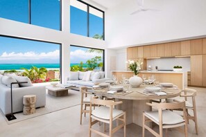A modern interior with a dining area, kitchen, and large windows overlooking a beach.