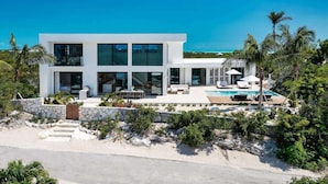 Une maison moderne à deux étages avec une piscine, entourée d’une végétation tropicale.