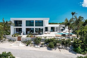 A modern two-story house with a pool, surrounded by tropical vegetation.