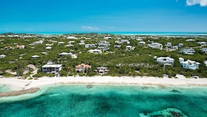 Vue aérienne d’une zone côtière avec de nombreuses maisons, une plage de sable et des eaux turquoise cristallines.