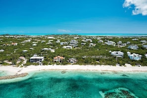 An aerial view of a coastal area with numerous houses, a sandy beach, and clear turquoise waters.