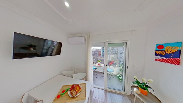 A modern apartment with a dining area, a TV mounted on the wall, a balcony with a view of buildings, and a colorful painting on the wall. - PREMIUM HABITAT LA RIERA (Pineda de Mar)