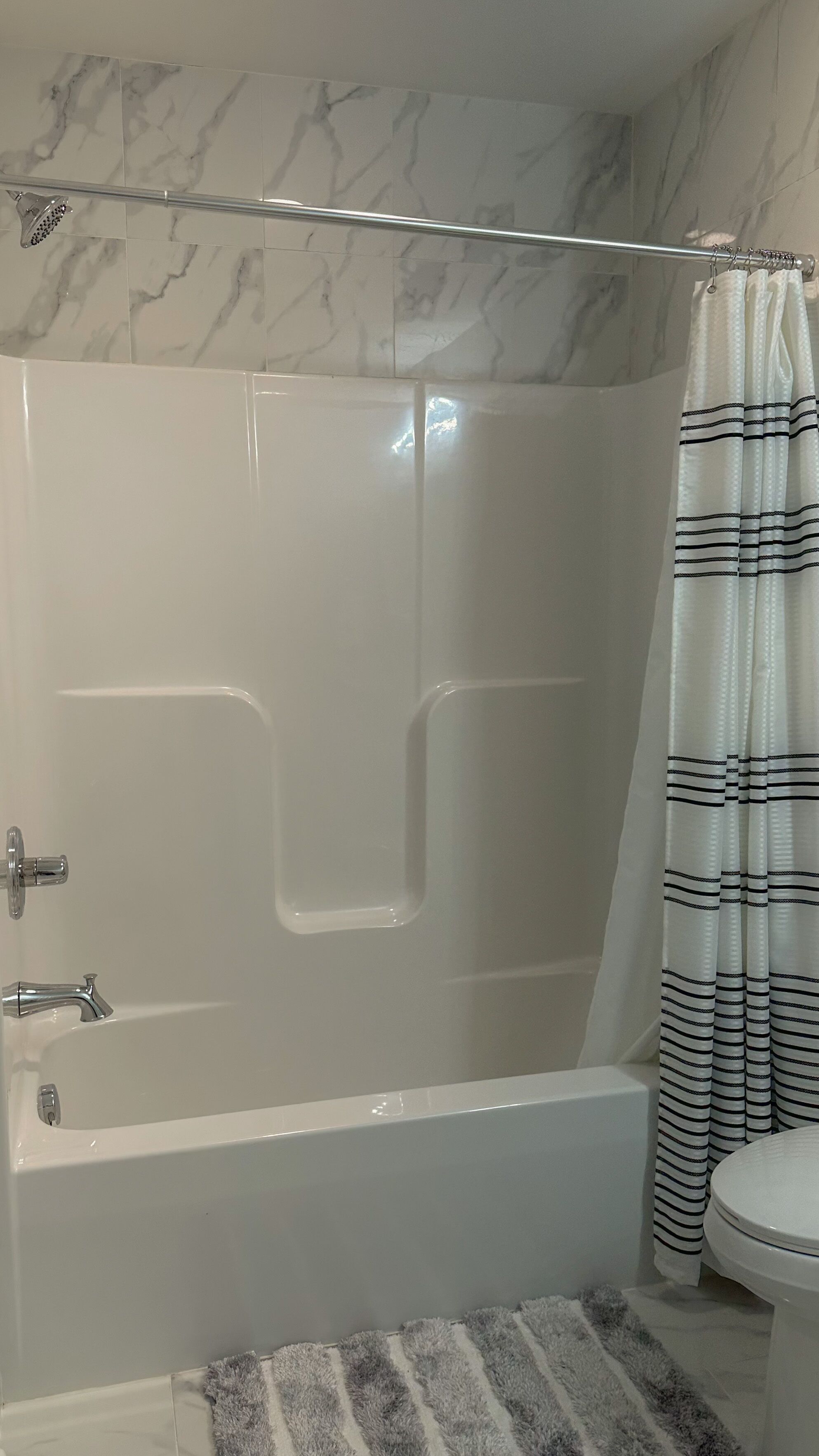 Een badkamer met een douche met glazen wand, een witte badkuip, een toilet en een badgordijn met strepen.