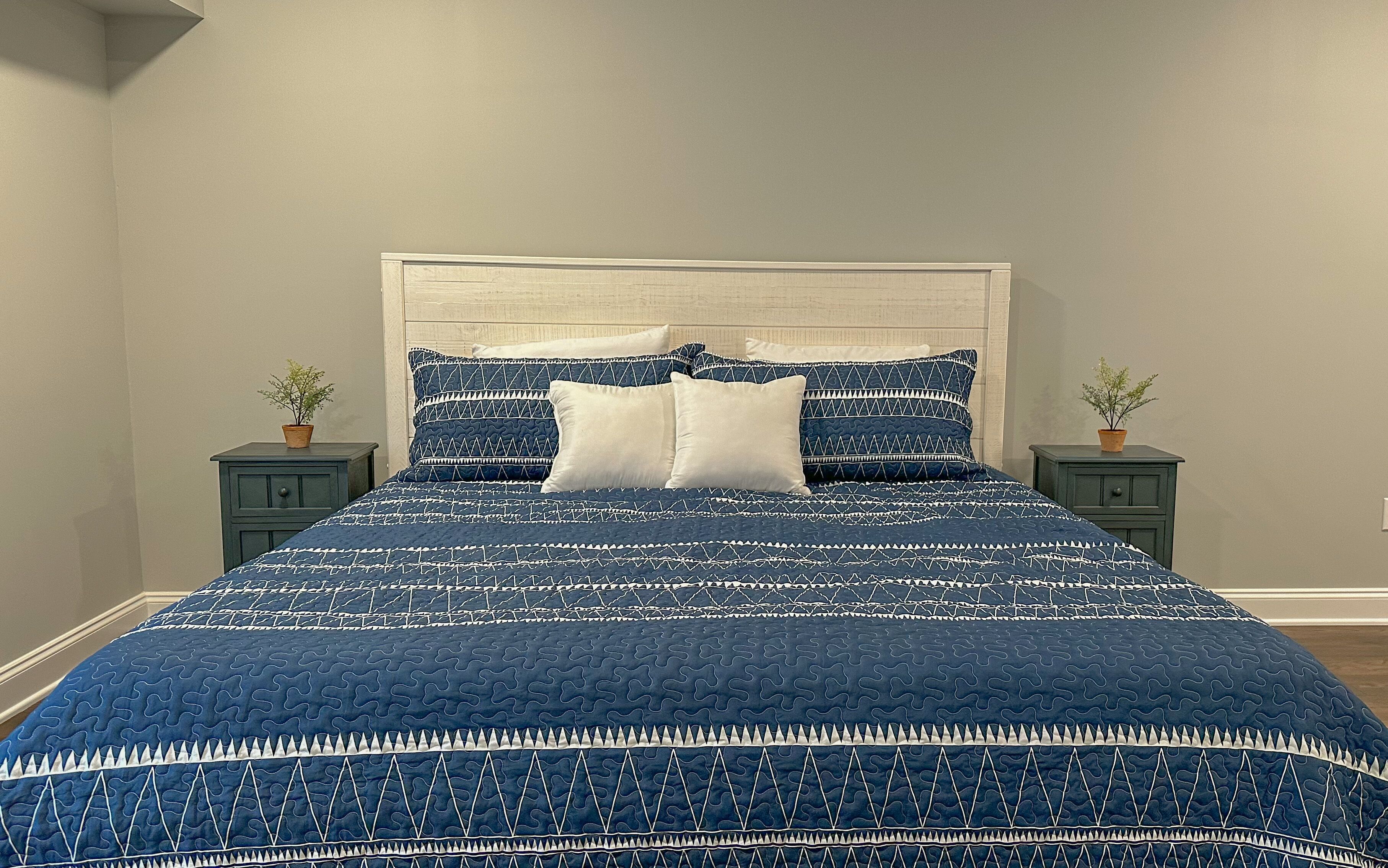 A bed with a blue patterned bedspread and white pillows, flanked by two nightstands with small potted plants.