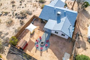 An aerial view of a house with a blue roof, a fenced backyard, and a circular seating area with red chairs.