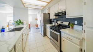 Eine moderne Küche mit weißen Schränken, einem Edelstahl-Kühlschrank, einem Gasherd und einer gefliesten Rückwand.
