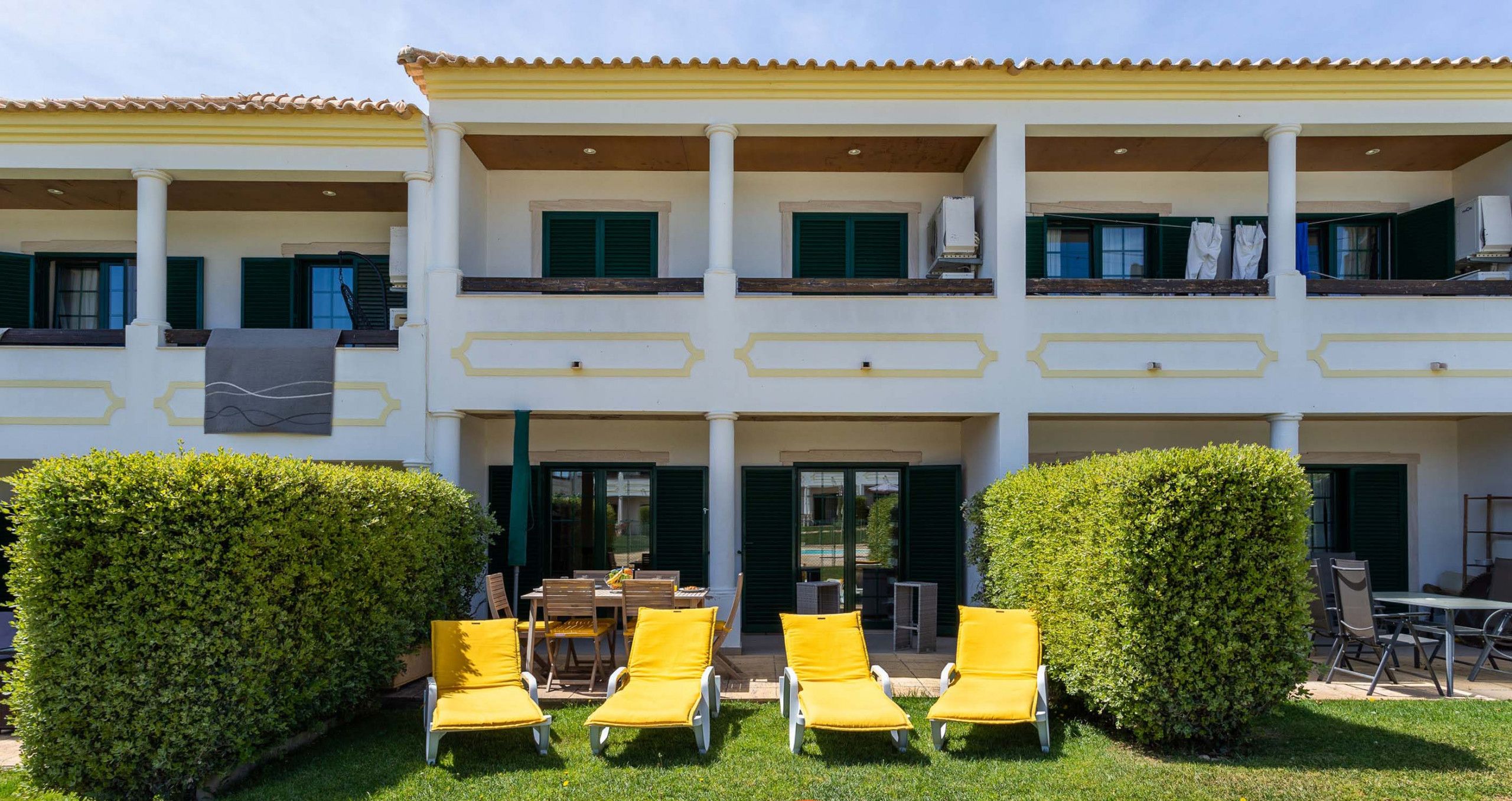 A two-story building with a balcony, yellow lounge chairs, and a well-maintained lawn.