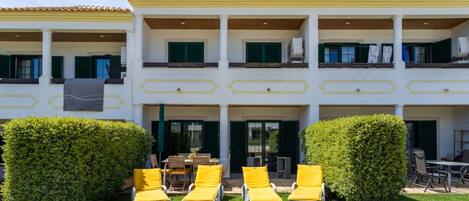 A two-story building with a balcony, yellow lounge chairs, and a well-maintained lawn.