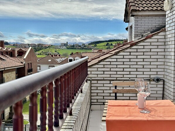 Uma varanda com vista para uma aldeia, um muro de tijolos e uma mesa com um copo de água.