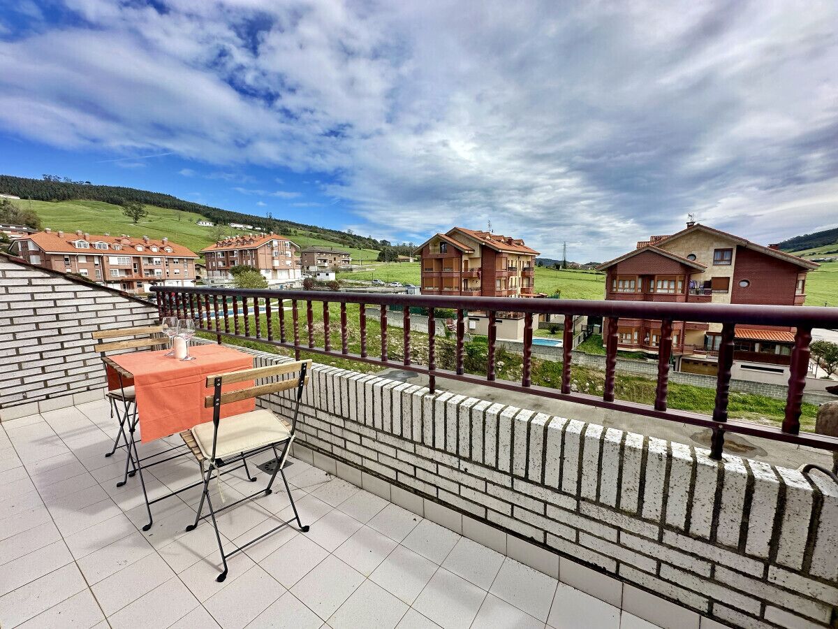 A balcony with a table and chairs, a brick wall, and a view of houses in the background.