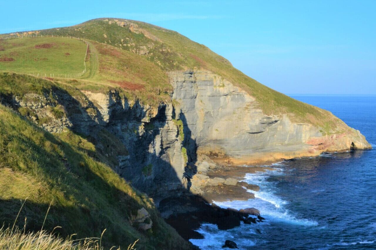 A coastal cliff with a grassy path leading up to a hill.