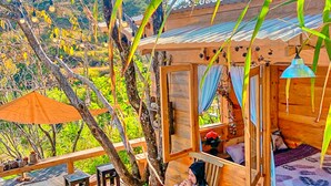 A wooden cabin with a porch, a hammock, and a bed with a patterned blanket. - Resort Pù luông Boutique Garden (Pu Luong)