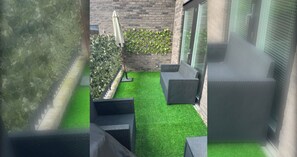 Un petit espace extérieur avec une pelouse artificielle, un mur en briques et une plante grimpante sur un treillage.