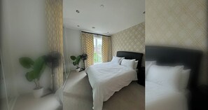 A hotel room with a bed, a potted plant, a standing fan, and a window with curtains.