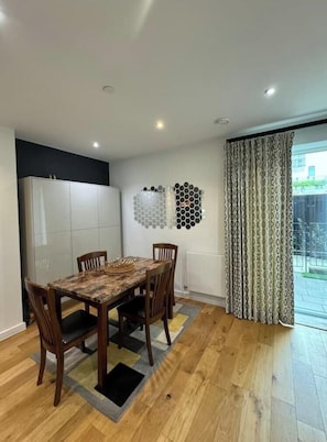 A dining area with a wooden table and chairs, a white cabinet, and a patterned curtain.
