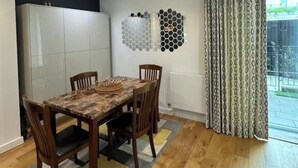 A dining area with a wooden table and chairs, a white cabinet, and a decorative wall piece. - Spacious & Family Friendly | 3 Beds | Stratford (London)