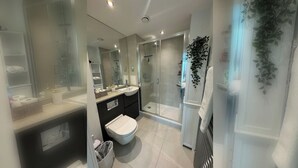 A modern bathroom with a glass shower enclosure, a white sink, and a toilet. - Spacious & Family Friendly | 3 Beds | Stratford (London)