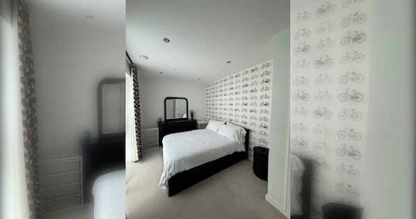 A bedroom with a bed, a dresser, a mirror, and a wall with a bicycle pattern.