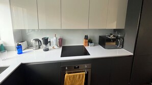 A modern kitchen with a black countertop, white cabinets, a built-in oven, and a coffee maker. - Spacious & Family Friendly | 3 Beds | Stratford (London)