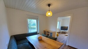 Un salon moderne avec une table à manger en bois, un canapé vert foncé et un petit téléviseur posé sur un meuble blanc.