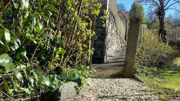 Un sentier pavé de petits cailloux mène à un bâtiment en pierre, entouré d’une clôture en bois.