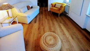 Un salon avec un canapé blanc, un fauteuil jaune, un pouf en osier et une lampe.