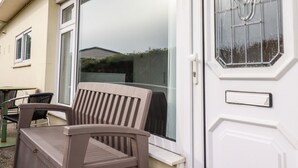 Una porta scorrevole in vetro con esterno bianco e un pannello di vetro, che dà accesso a un patio con una sedia di legno e un tavolino.