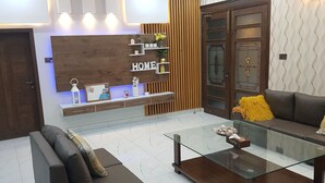 A modern living room with a glass coffee table, a brown sofa, and a wooden accent wall with the word "HOME". - Entire 6-bed Garden Villa (Chakswari)