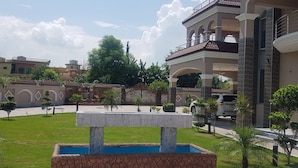 A courtyard with a fountain, a white car, and a building with multiple balconies and a stone facade. - Entire 6-bed Garden Villa (Chakswari)