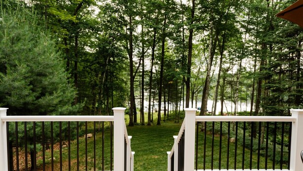 Terraza de madera con barandillas blancas que da vista a un bosque y una masa de agua.