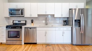 A modern kitchen with stainless steel appliances, white cabinetry, and a wooden floor.