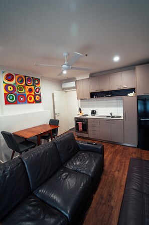 A modern kitchen with a refrigerator, stove, and microwave. There is a dining table with chairs and a black leather sofa.