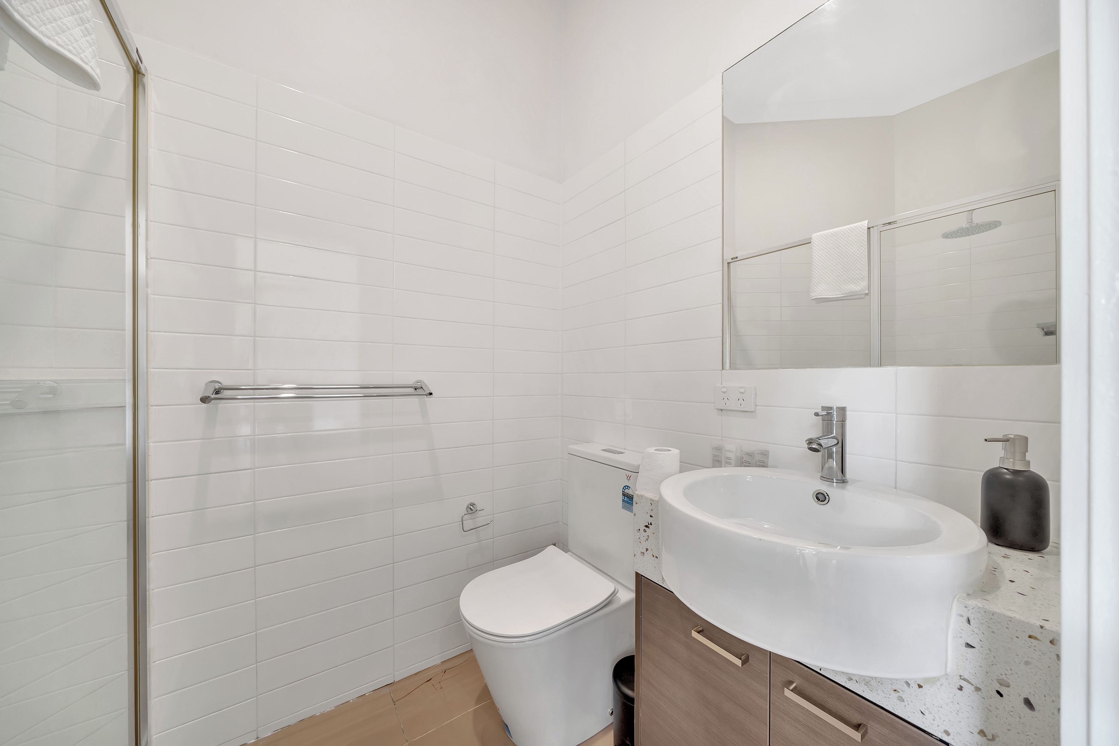 A modern bathroom with white tiles, a toilet, a sink with a mirror, and a shower area.
