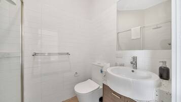 A modern bathroom with white tiles, a toilet, a sink with a mirror, and a shower area.