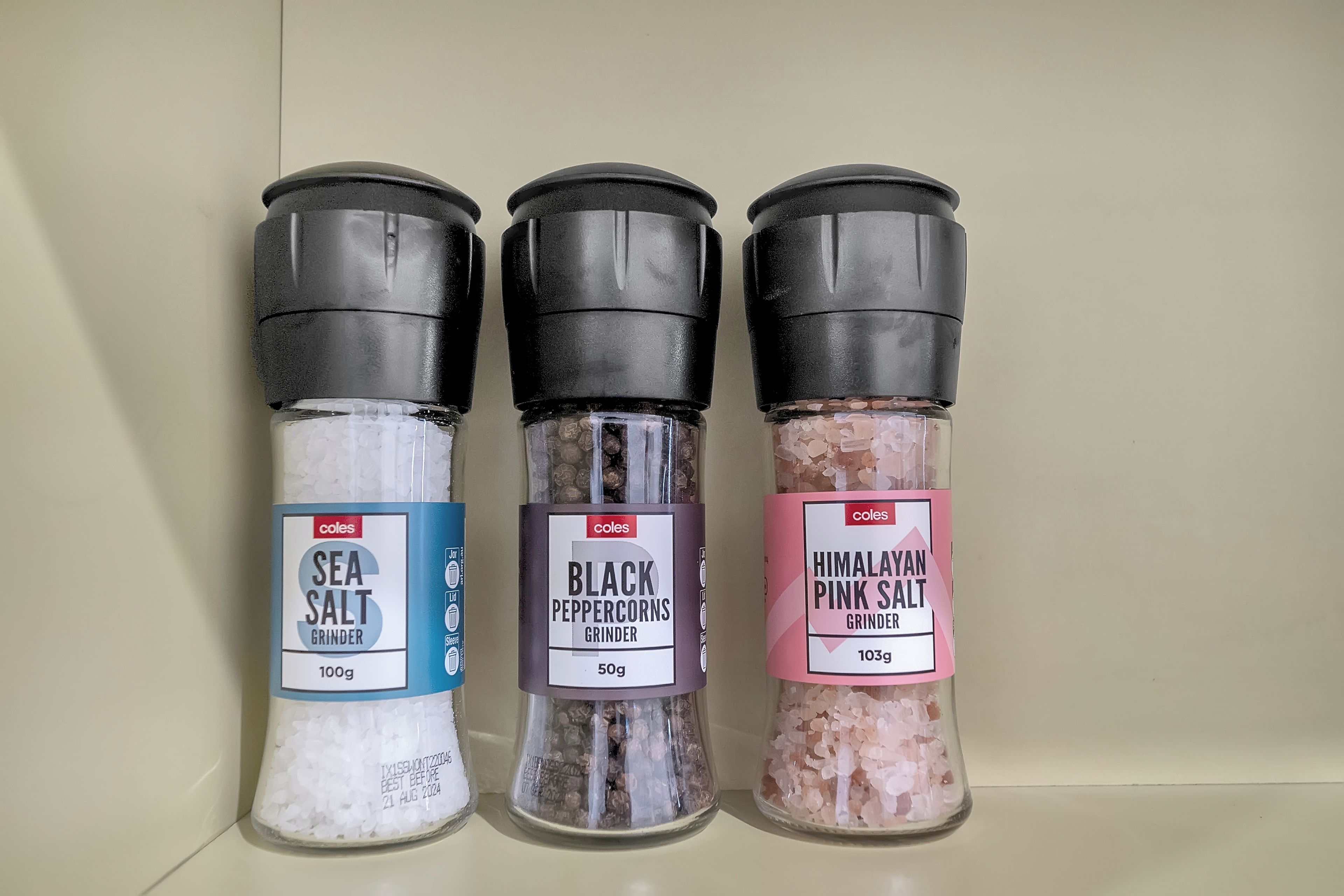 Three spice containers labeled 'Sea Salt', 'Black Peppercorns', and 'Himalayan Pink Salt' on a shelf.