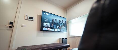 Quarto com televisão montada exibindo interface de serviço de streaming, mesa de massagem e uma porta.