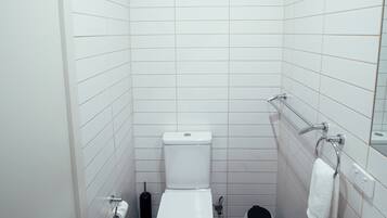 A small, modern bathroom with white tiles, a white toilet, a sink with a speckled countertop, and a towel rack.