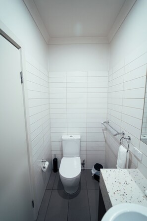 A small, modern bathroom with white tiles, a white toilet, a sink with a speckled countertop, and a towel rack.