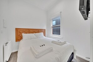 A bedroom with a wooden headboard, a large window, a radiator, and a wall-mounted phone.