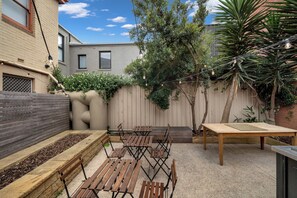 Un patio con mesas y bancos de madera, suelo de hormigón y valla de madera.